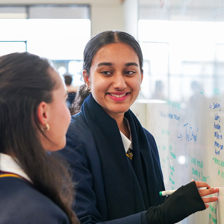 Student writing on the whiteboard in the classroom at Students reading a book in the library at St John XXIII College Stanhope Gardens